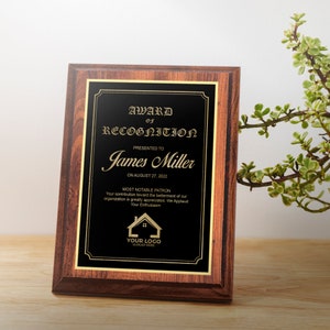 May include: A brown wooden plaque with a gold trim and a black background. The plaque has a gold inscription that reads "Award of Recognition" presented to "James Miller" on August 27, 2022. The inscription also includes the text "Most Notable Patron" and a small house logo with the text "Your Logo" and "Slogan Here".
