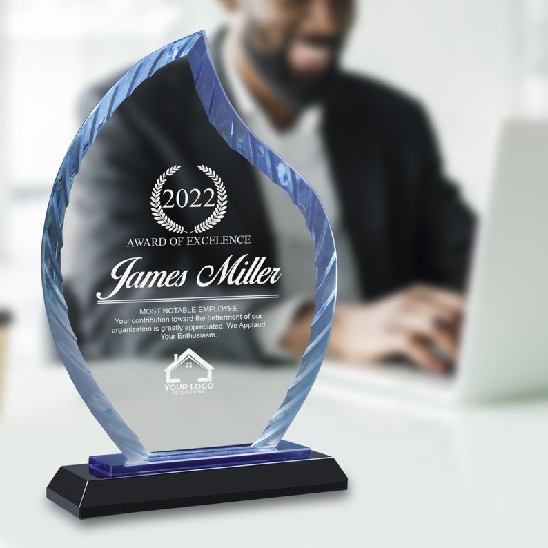 May include: A blue glass award in the shape of a flame with a black base. The award reads "2022 Award of Excellence" and "James Miller" with the text "Most Notable Employee" below. The text continues, "Your contribution toward the betterment of our organization is greatly appreciated. We Applaud Your Enthusiasm."