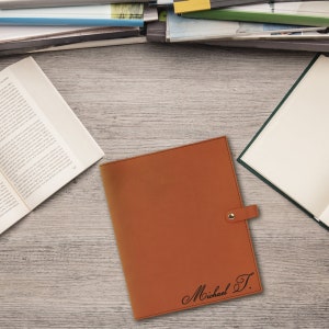 May include: A brown leather folder with a gold snap closure and a personalized inscription that reads "Michael T."