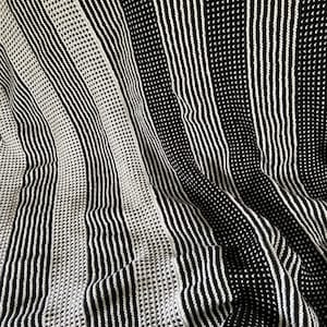 Puede incluir: Manta de tiro a rayas blancas y negras con un patrón texturizado. La manta está doblada y tiene un aspecto suave y acogedor.