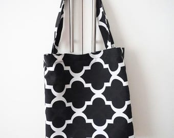 Könnte beinhalten: Eine schwarz-weiße Tragetasche mit einem geometrischen Vierpassmuster. Die Tasche hat zwei Griffe und hängt vor einem weißen Hintergrund. Die Tasche ist aus Stoff und wird wahrscheinlich zum Tragen von Gegenständen verwendet.