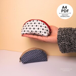 Könnte beinhalten: Zwei kleine, halbmondförmige Stoffbeutel. Der obere Beutel ist weiß mit schwarzen und grauen Sternen, einem roten Reißverschluss und einem roten Innenfutter. Der untere Beutel ist marineblau mit einem weißen geometrischen Muster und einem beigen Reißverschluss.