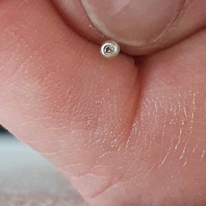 Op de afbeelding: Een kleine, zilveren kraal met een klein gaatje in het midden.