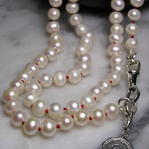 May include: A white pearl necklace with a silver pendant. The necklace is strung on red thread and has a silver clasp.