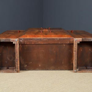 May include: A large, rectangular wooden trunk with a rich, reddish-brown finish. The trunk features a hinged lid with several small, round knobs and is supported by four sturdy legs. The overall design suggests a vintage or antique style.
