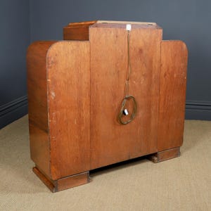 May include: A vintage wooden cabinet with a light brown finish. The cabinet has a rectangular shape with rounded edges and a small rectangular top. A power cord with a plug is visible on the back.