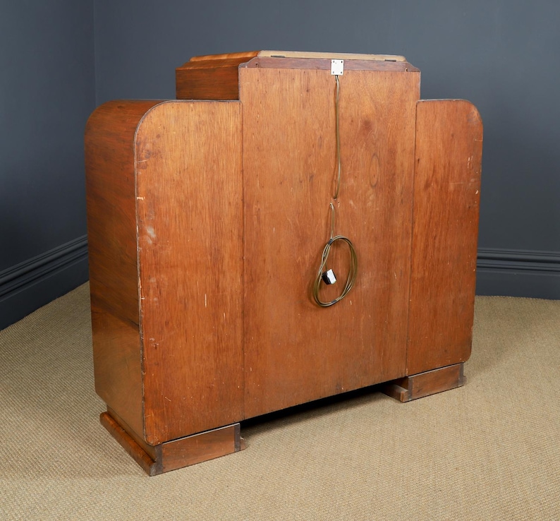 May include: A vintage wooden cabinet with a light brown finish. The cabinet has a rectangular shape with rounded edges and a small rectangular top. A power cord with a plug is visible on the back.