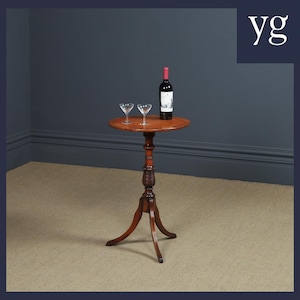 May include: A small, round, wooden table with a turned pedestal base and three legs. Two glasses and a bottle of wine are on the table top.