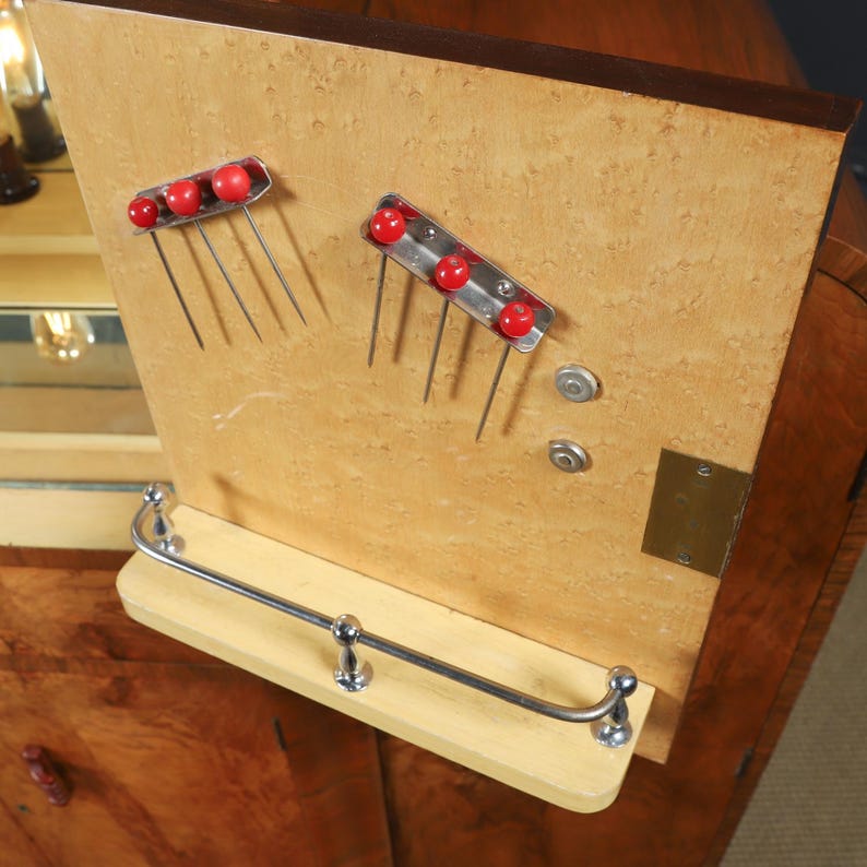 May include: Close-up of a wooden cabinet interior with two metal and red decorative hair combs. A small metal bar and shelf are below the combs. The cabinet has a light wood grain finish.