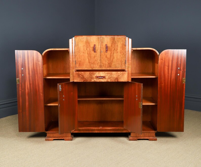 May include: A large, vintage wooden cabinet with multiple storage compartments. The cabinet features a central section with a drop-down desk and two side sections with open shelving. The doors and drawers have brass hardware. The wood has a rich, reddish-brown color.