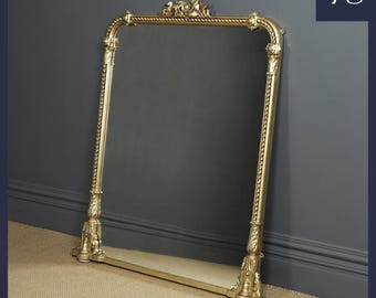 May include: A gold-toned ornate mirror with a decorative top and a beveled edge. The mirror has a shelf at the bottom.