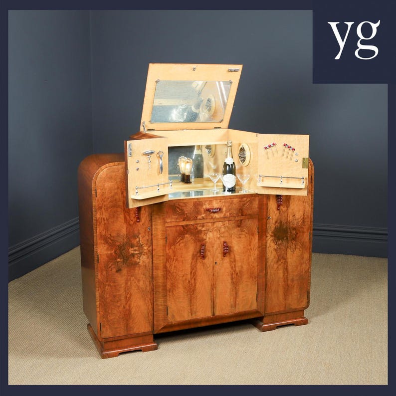 May include: A vintage wooden bar cabinet with a mirrored interior and a fold-out design. The cabinet features a rich, warm wood grain finish and includes a bottle of champagne, glassware, and bar tools. The cabinet is a stylish piece of furniture.