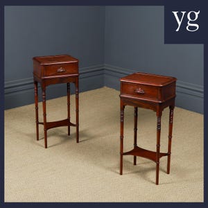 May include: A pair of antique mahogany side tables. Each table has a rectangular top with a drawer and an ornate pull. They stand on slender, turned legs with a lower shelf. The tables are a rich, warm brown colour.