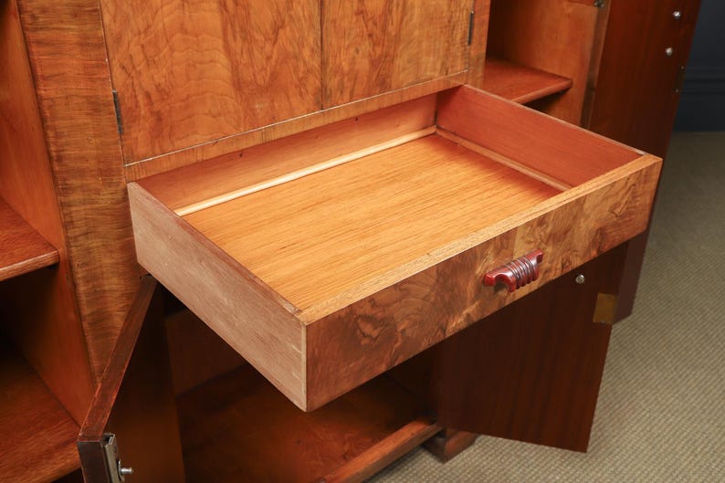 May include: A wooden cabinet with an open drawer. The drawer is made of light-colored wood with a reddish-brown handle. The cabinet has a rich, warm wood grain finish, and the drawer is partially extended.