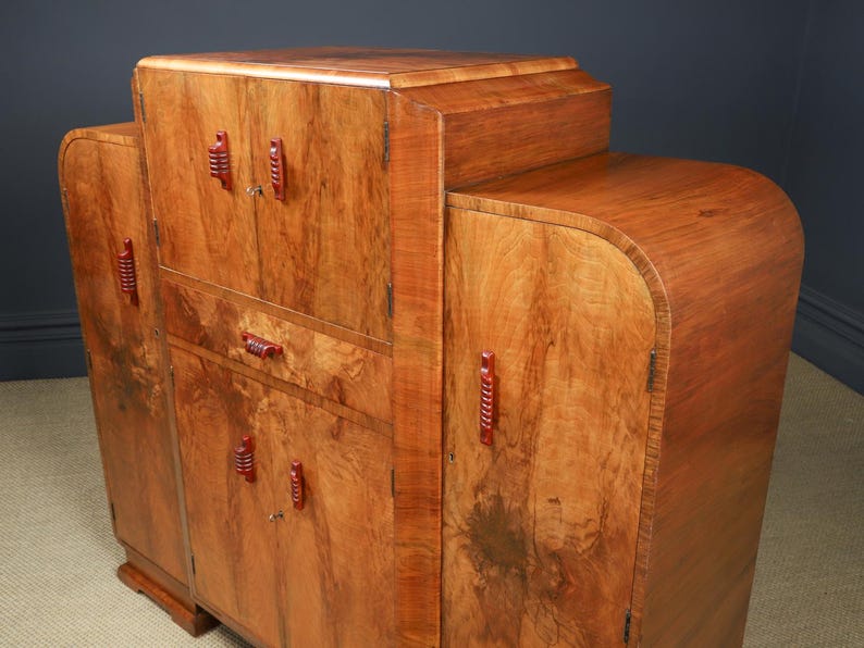 May include: A wooden cabinet with a warm, reddish-brown finish. The cabinet has a curved design with multiple doors and drawers. Red handles and pulls provide a contrasting accent. The wood grain is visible throughout the piece.