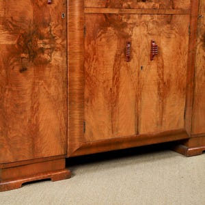 May include: A vintage wooden cabinet with a warm, reddish-brown finish. The cabinet features a symmetrical design with doors, drawers, and decorative handles. The wood grain is prominent, adding to its classic appeal. The cabinet sits on a sturdy base.