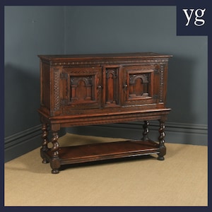 Puede incluir: Un armario de madera marrón oscuro con dos puertas talladas y un estante inferior sostenido por patas torneadas. El armario tiene un diseño sencillo y tradicional.