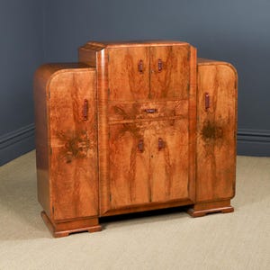 May include: A vintage wooden cabinet with a warm, reddish-brown finish. The cabinet features a central section with doors and a drawer, flanked by curved side panels. It has decorative hardware and a stepped top.