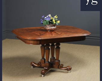 May include: A dark wood table with a geometric inlay pattern on the top. The table has a pedestal base with four turned legs and four castors. A small copper planter with colorful flowers sits on the table.