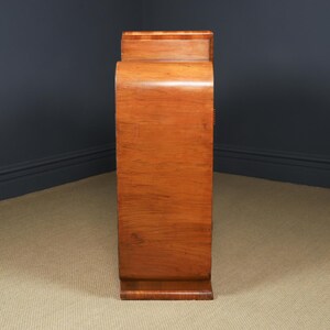 May include: A tall, wooden cabinet with a curved front and a warm, reddish-brown finish. The cabinet has a rectangular base and a slightly recessed top. The wood grain is visible, adding to its vintage appeal. The cabinet is likely used for storage.