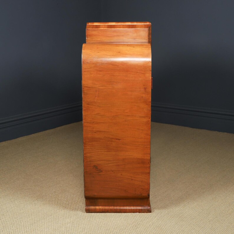 May include: A tall, wooden cabinet with a curved front and a warm, reddish-brown finish. The cabinet has a rectangular base and a slightly recessed top. The wood grain is visible, adding to its vintage appeal. The cabinet is likely used for storage.