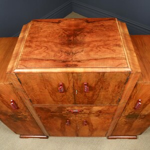 May include: A wooden cabinet with a rich, warm brown finish. The cabinet has a rectangular top and curved sides, with red-toned handles. The wood grain is prominent, adding to its vintage appeal. It features multiple doors and drawers.