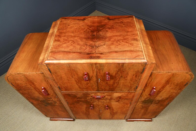 May include: A wooden cabinet with a rich, warm brown finish. The cabinet has a rectangular top and curved sides, with red-toned handles. The wood grain is prominent, adding to its vintage appeal. It features multiple doors and drawers.