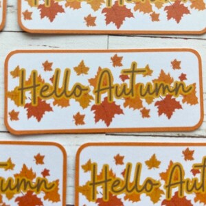 May include: A set of four rectangular stickers with a white background and orange borders. Each sticker features a design of orange and brown maple leaves with the text "Hello Autumn" in a yellow font.