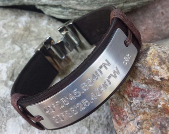 May include: A brown leather bracelet with a silver metal plate engraved with coordinates: 40°28'45.6640"N 90°38'28.4090"W.