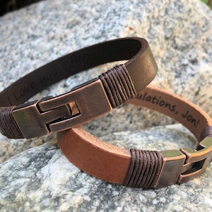 May include: Two brown leather bracelets with metal clasps. One bracelet is engraved with "I love you Offi", and the other is engraved with "Congratulations, Jon!"