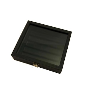 May include: A black wooden display case with a glass top and a metal latch. The case has a black velvet interior and is designed to hold and display small items.
