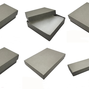 May include: Gray rectangular gift boxes in various orientations. One box is open, revealing white padding inside. The boxes are made of a textured material and are suitable for jewelry or small gifts.