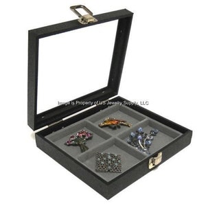 May include: Black jewelry box with a glass lid and a lock. The box has five compartments lined with gray felt and contains four brooches.