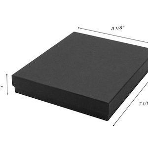 May include: A rectangular black gift box with a lid. The box features printed dimensions of 5 1/8 inches in width, 7 1/8 inches in length, and 1 1/8 inches in height, indicated by black arrows on the sides of the object against a white background.