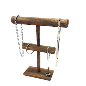 May include: Wooden jewelry stand with three tiers for displaying necklaces, bracelets, and rings. The stand is made of dark brown wood and has a simple, elegant design.