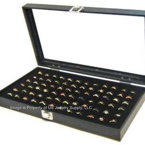 May include: Black ring display box with a glass top and black velvet lining. The box is filled with rings.