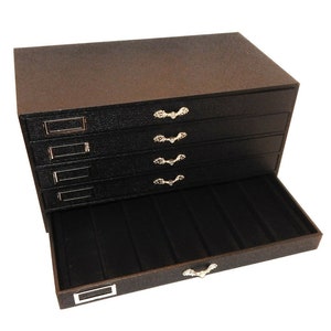 May include: Black jewelry box with five drawers and a pull-out tray. The drawers have silver-colored handles and labels. The tray has a silver-colored handle.
