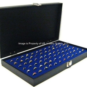 May include: Black ring display case with a blue velvet interior. The case has a hinged lid and a lock. The case is filled with rings.