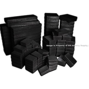 May include: A large quantity of black jewelry boxes stacked in a pile. The boxes are made of cardboard and have a smooth, black finish.