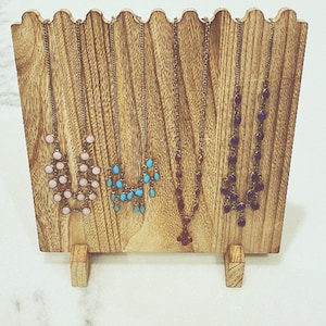 May include: Five necklaces displayed on a wooden stand. The necklaces feature different colored beads, including pink, turquoise, and purple.