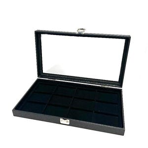 May include: Black velvet-lined jewelry display box with a clear glass lid and 12 compartments. The box is closed and sitting on a white surface.