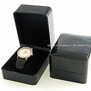 May include: Two black faux leather watch boxes. One box is open and a gold watch with a white face is inside. The watch has a diamond-like bezel.