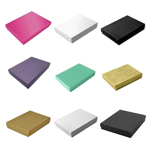 May include: Nine different colored gift boxes. The boxes are all the same size and shape, but they have different colors and textures. The colors include pink, white, black, purple, green, gold, brown, white with a textured pattern, and black with a textured pattern.