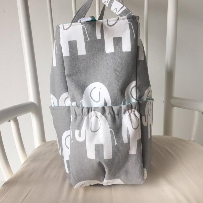 May include: A gray fabric storage bin with white elephant designs. The bin has multiple pockets and a drawstring closure.
