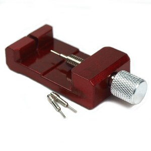 May include: A watch band link remover tool with a dark red wooden base and a silver metal screw and pin. Two additional silver pins are included. The tool is designed for watch repair and adjustment.