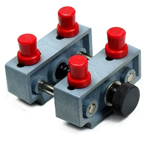 May include: A gray metal watchmaker's vise with four red knobs and a black knob. The vise is used to hold a watch or other small object securely while working on it.