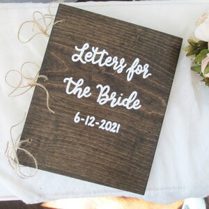 Puede incluir: Una caja de madera con un acabado r&uacute;stico marr&oacute;n y letras blancas que dicen "Letters for the Bride 6-12-2021". La caja est&aacute; atada con cuerda y es un regalo de boda para la novia.