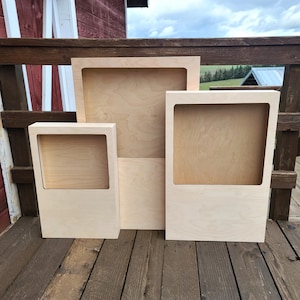 May include: Three wooden frames of different sizes, all with a natural wood finish. The frames are standing on a wooden deck.