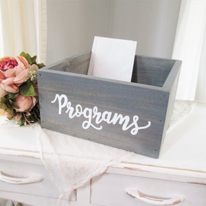 May include: A gray wooden box with the word "Programs" written in white on the front. The box is sitting on a white table with a white cloth on top.