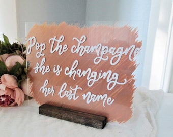 Pop the champagne she's changing her last name, bridal shower acrylic sign, bride to be, champagne mimosa bar sign, bachelorette party sign